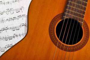 A close-up of a classical guitar with sheet music partially tucked under its strings.