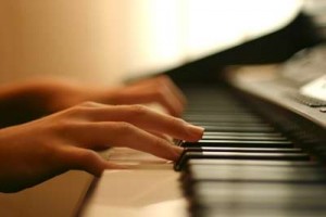 Close-up of hands playing a piano keyboard in warm, soft lighting.