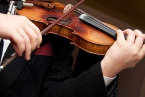 A musician in formal attire playing a violin with a bow in motion.