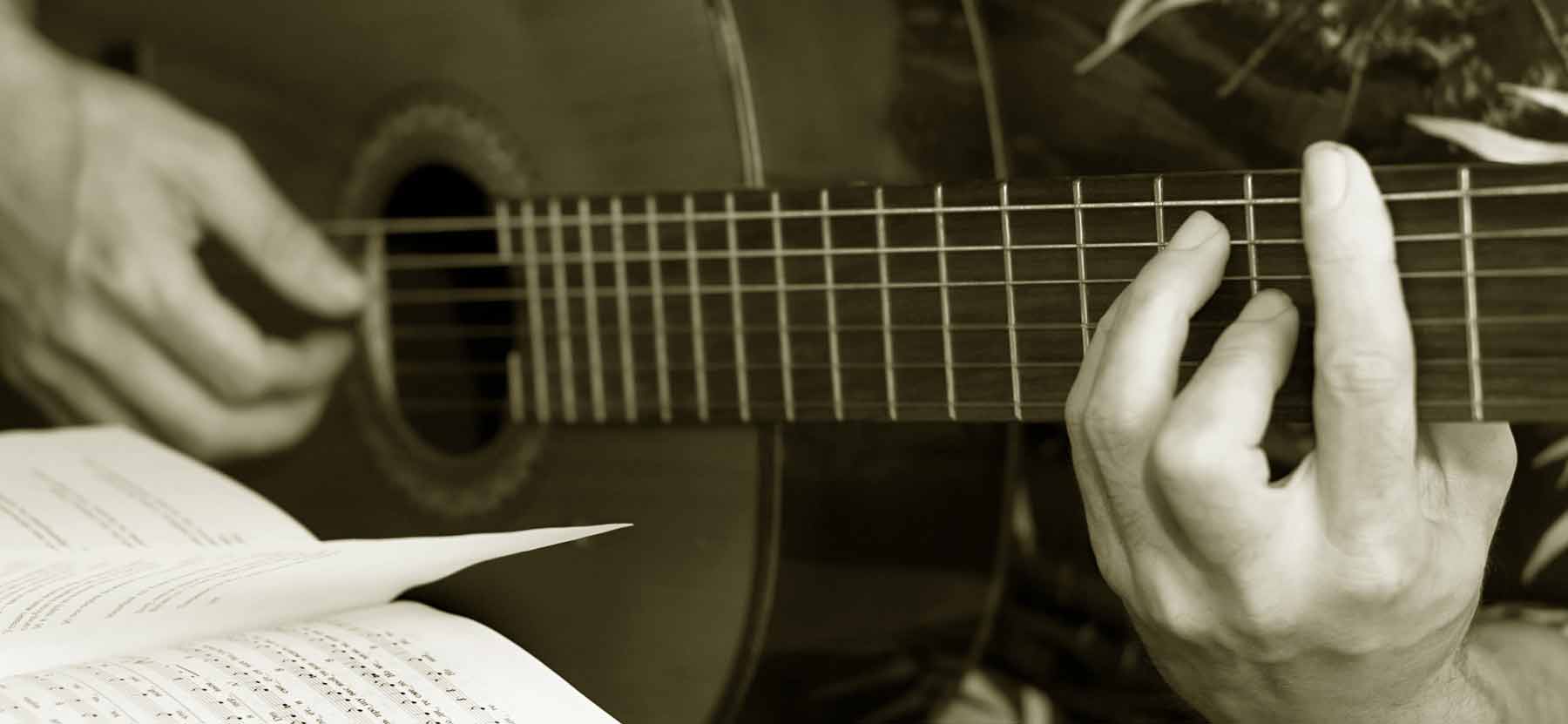 A musician playing an acoustic guitar with sheet music open in front of them.