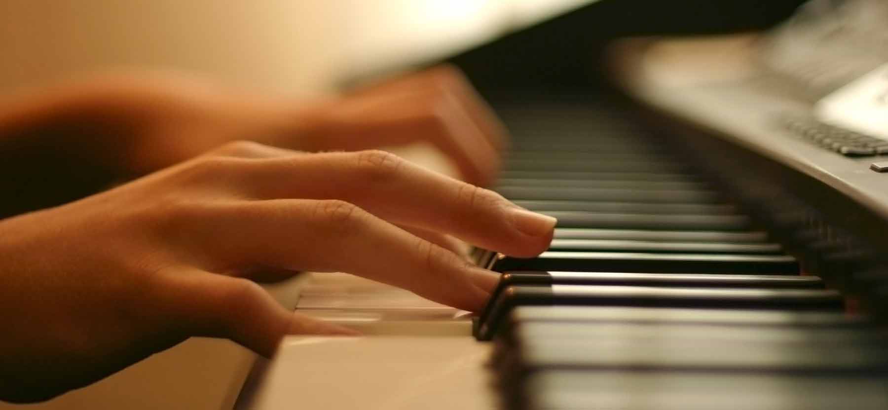 Close-up of hands playing a piano keyboard in warm, soft lighting.