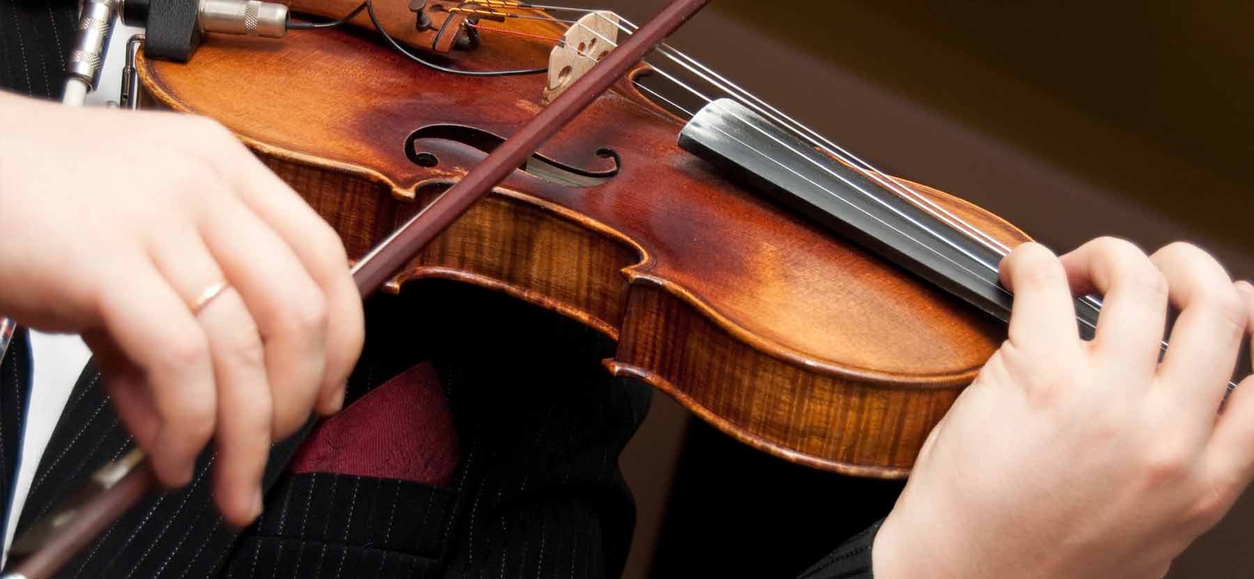 A violinist in formal attire playing a wooden violin with a bow in motion.